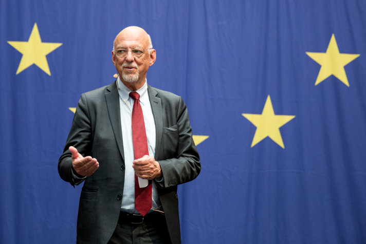 Hans Dahlgren står och talar med en stor bakgrund med EU-flaggan målad på.